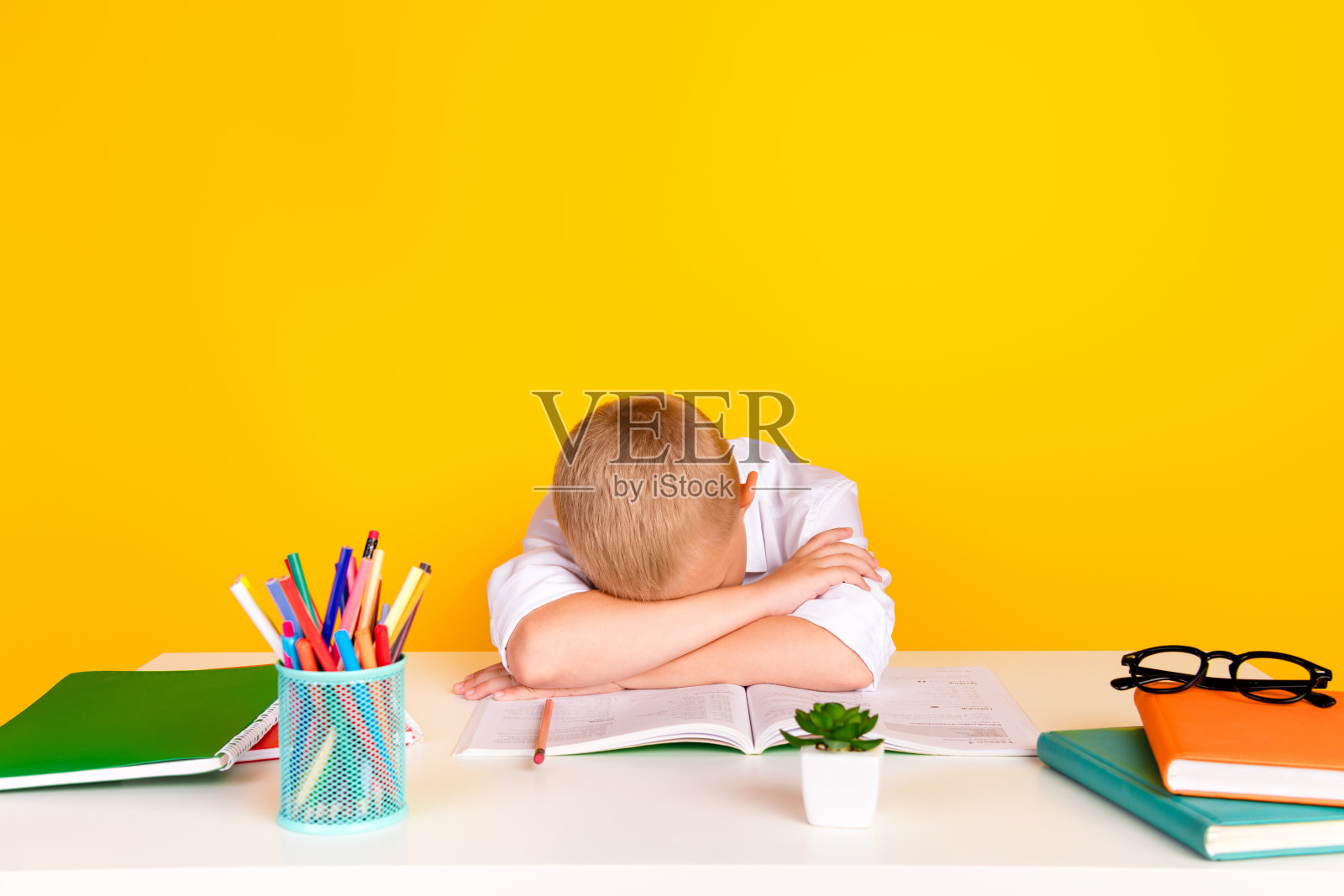 迷人可爱的困倦男孩坐在书桌上做作业练习，在黄色背景下独自入睡照片摄影图片