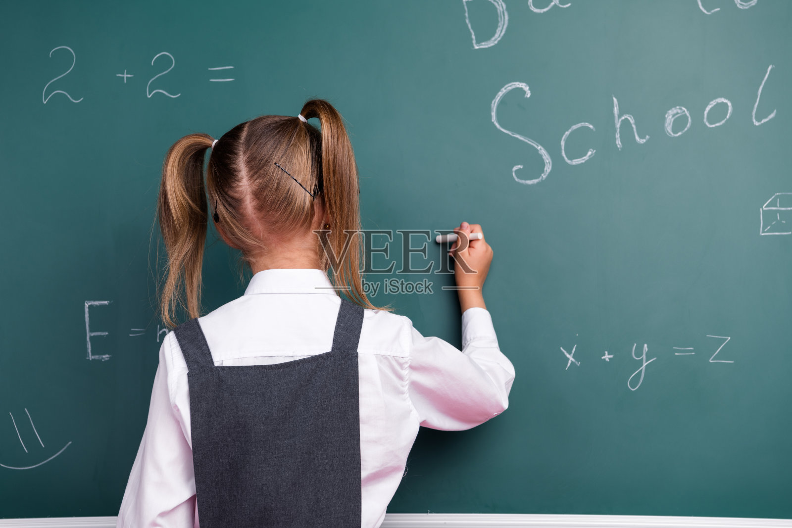 照片中迷人的小女生用粉笔答课，穿着时髦的校服教室黑板背景照片摄影图片