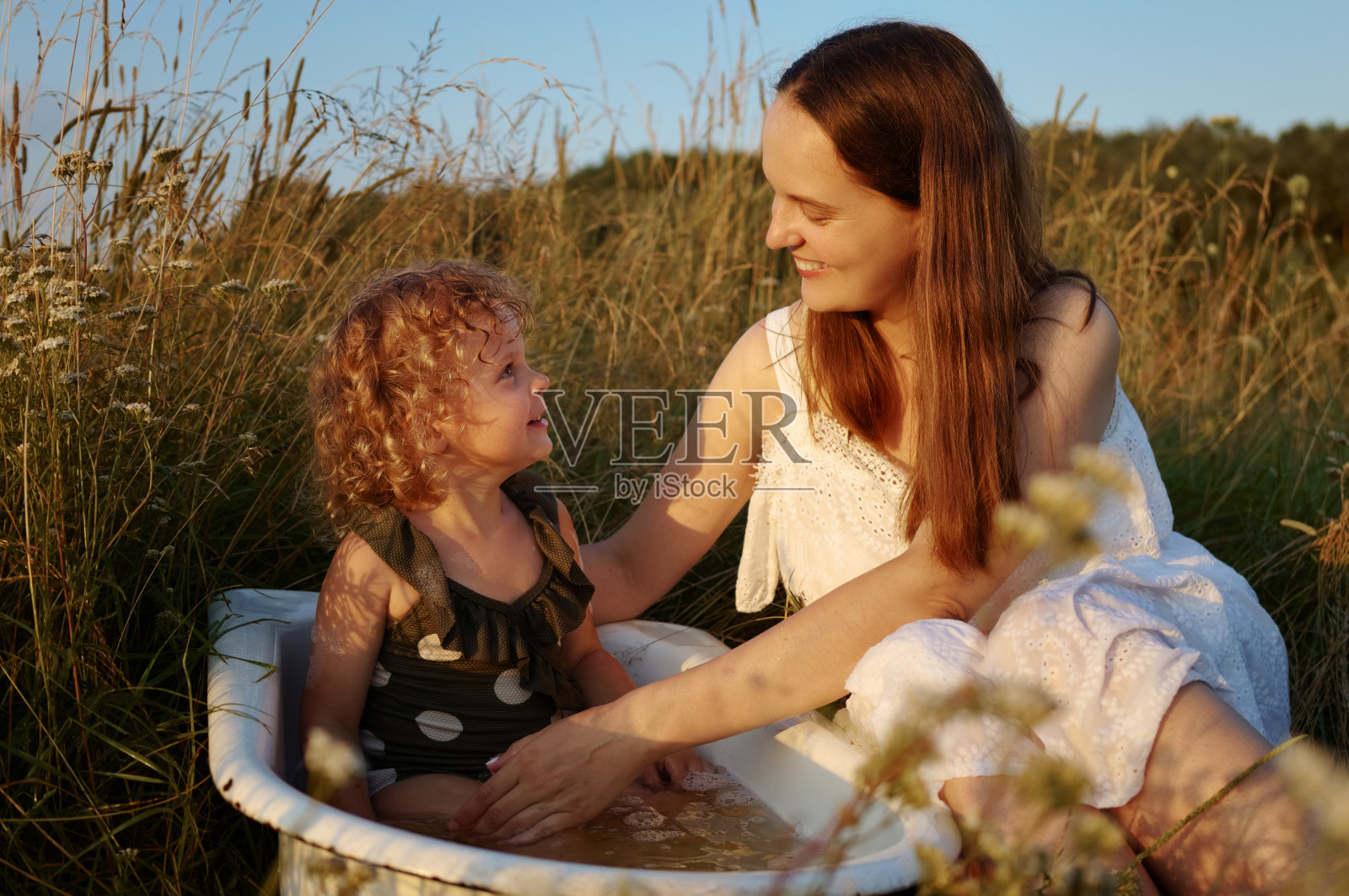 小微笑可爱开朗的女孩和她的妈妈在老式水槽里洗澡时体验幸福，在阳光明媚的田野背景下享受户外的乐趣照片摄影图片