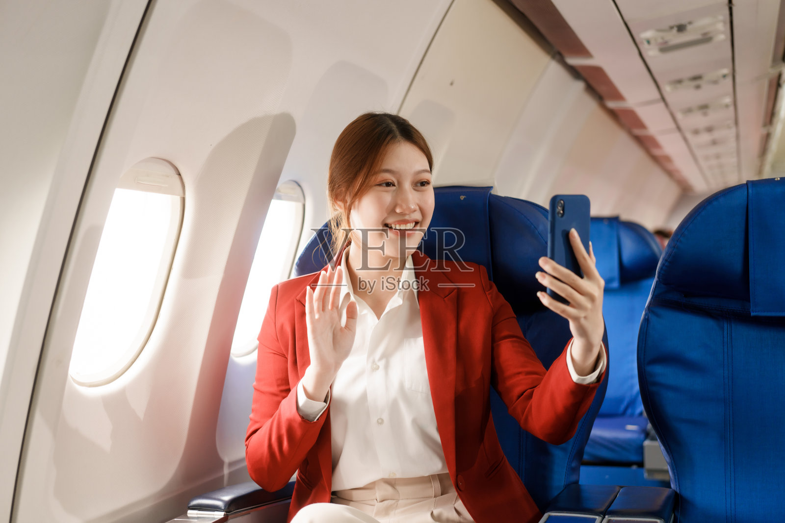 一位亚洲女商人乘飞机出国旅行，坐在靠窗的座位上。她看书，用电脑，用她的航空公司信用卡有效地管理旅行费用。照片摄影图片