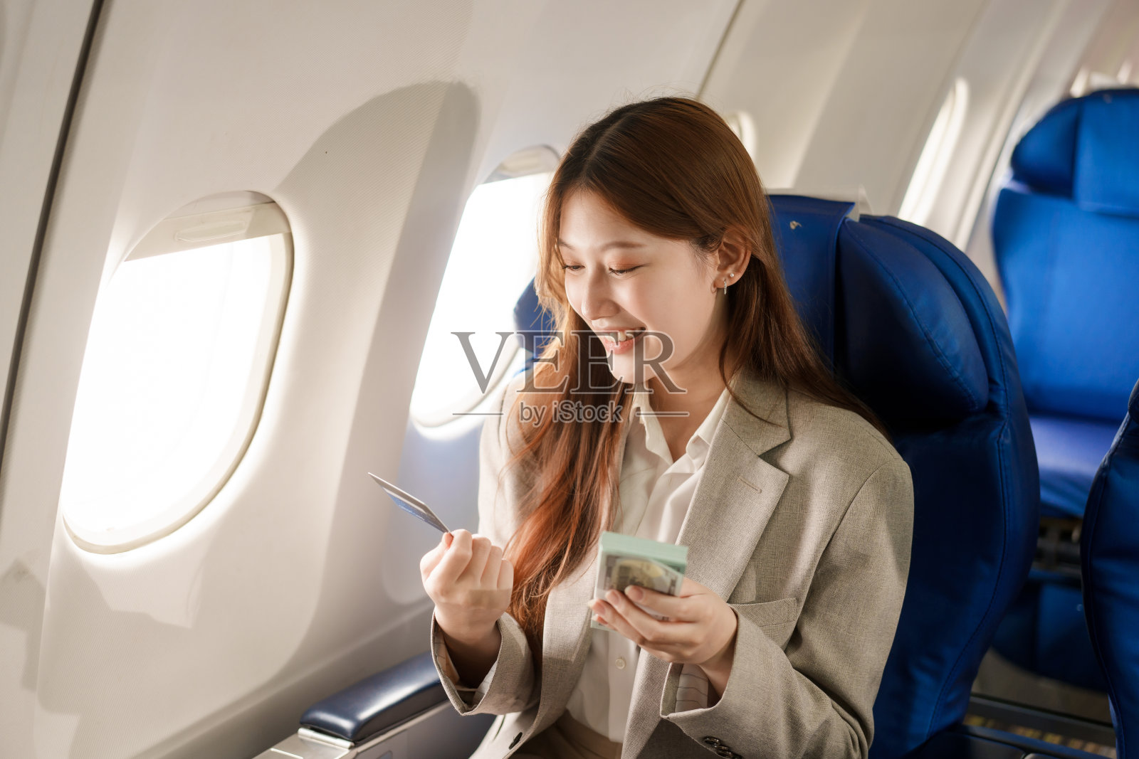 一位亚洲女商人乘飞机出国旅行，坐在靠窗的座位上。她看书，用电脑，用她的航空公司信用卡有效地管理旅行费用。照片摄影图片