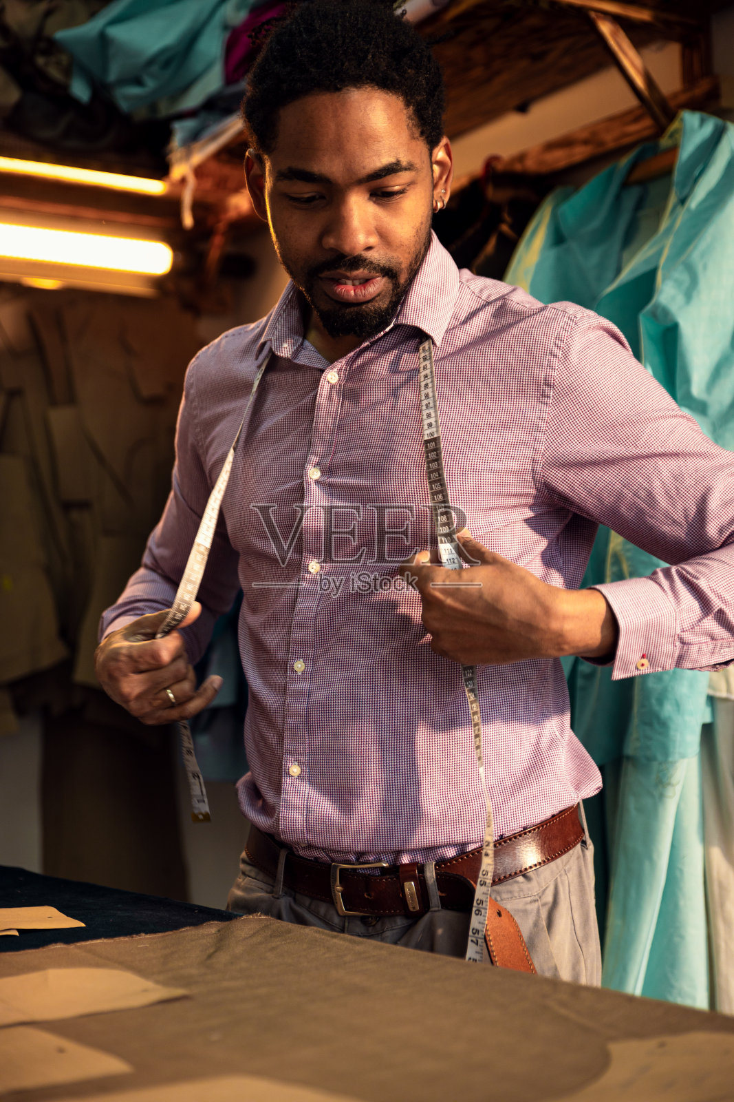 一位男时装裁缝在他的车间里为西装设计量尺寸。照片摄影图片