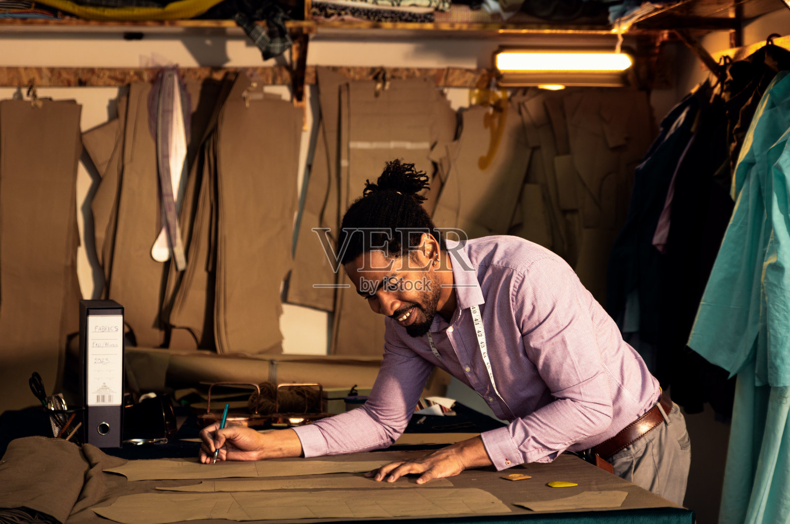 一位男时装裁缝在他的车间里为西装设计量尺寸。照片摄影图片