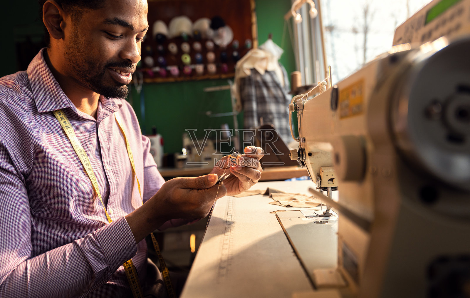 一位男时装裁缝在他的车间里为设计西装而在缝纫机上工作。照片摄影图片