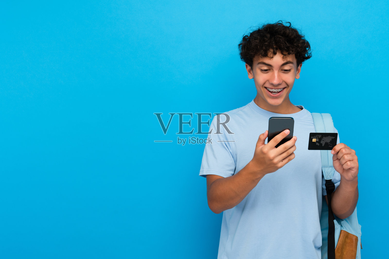 兴奋的小学生背着背包，拿着信用卡和手机，孤立在背景中照片摄影图片