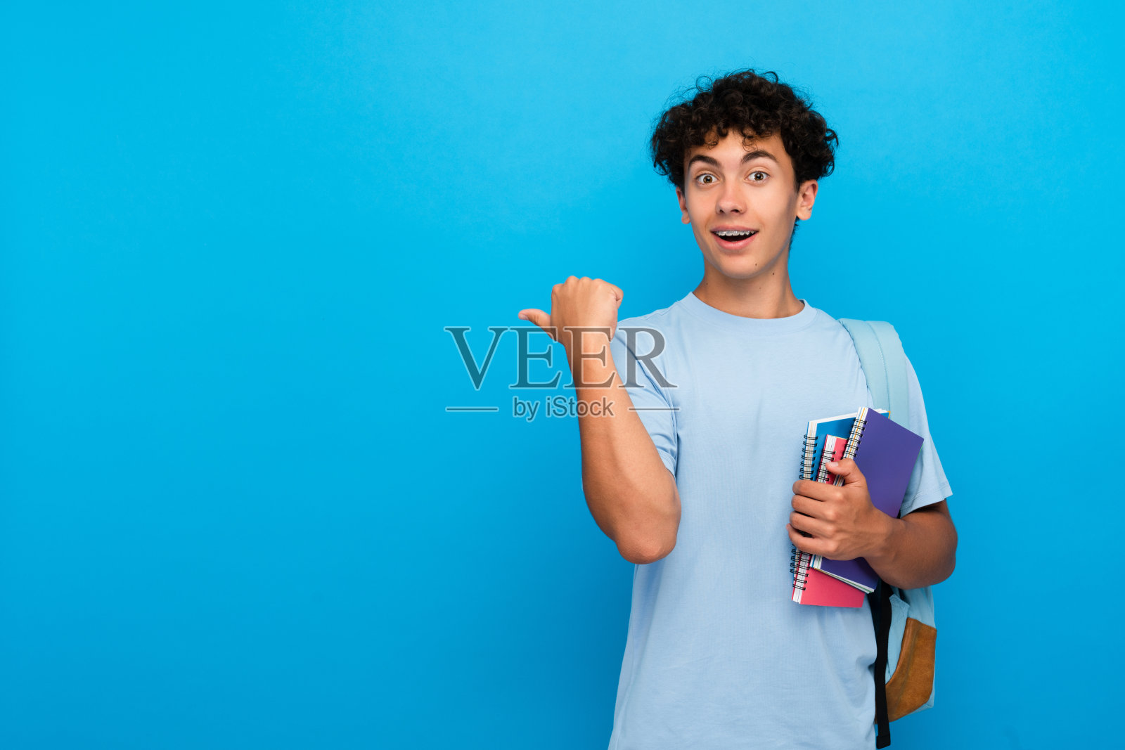 惊讶的男孩小学生学生少年拿着书包，手里拿着书，用手指着空白的复印空间照片摄影图片