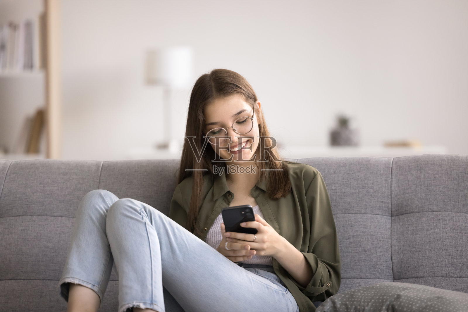 微笑的少女放松地使用智能手机，与朋友聊天照片摄影图片