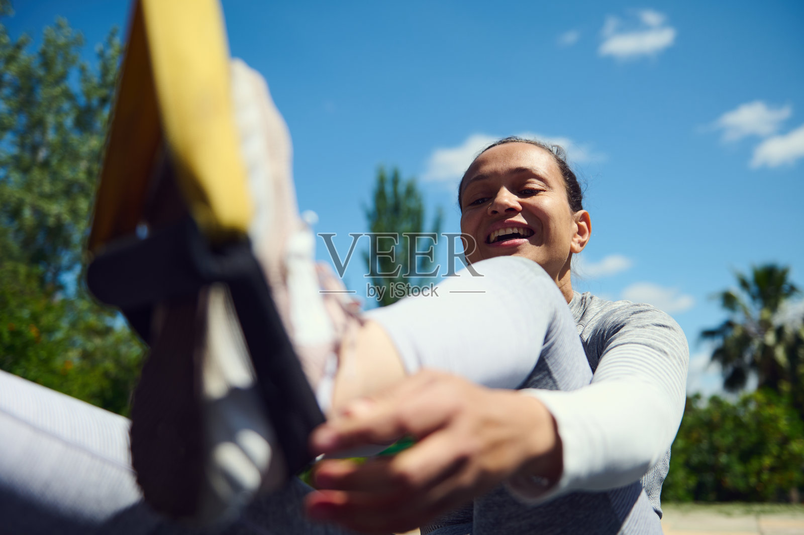 年轻女子在公园里进行户外锻炼，在阳光明媚的日子里用健身带伸展身体，展现活力和健康照片摄影图片