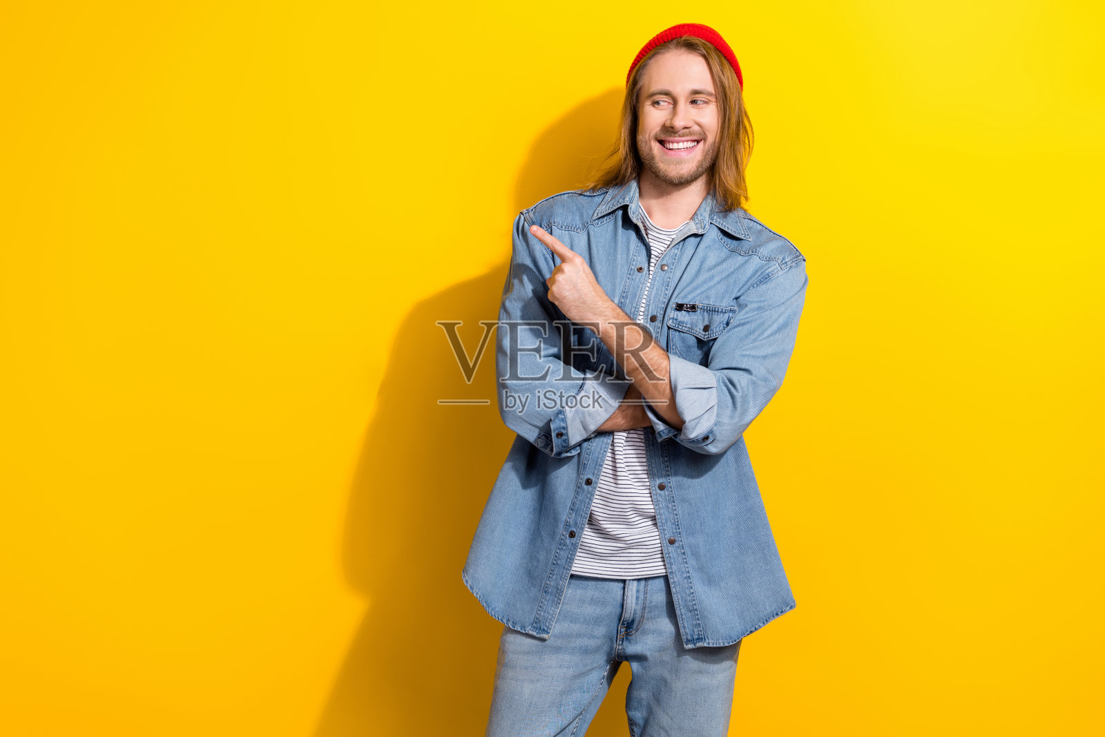时髦的积极男子的肖像，鲍勃发型，穿着牛仔夹克，看起来直接指向销售空间，孤立在黄色背景上照片摄影图片