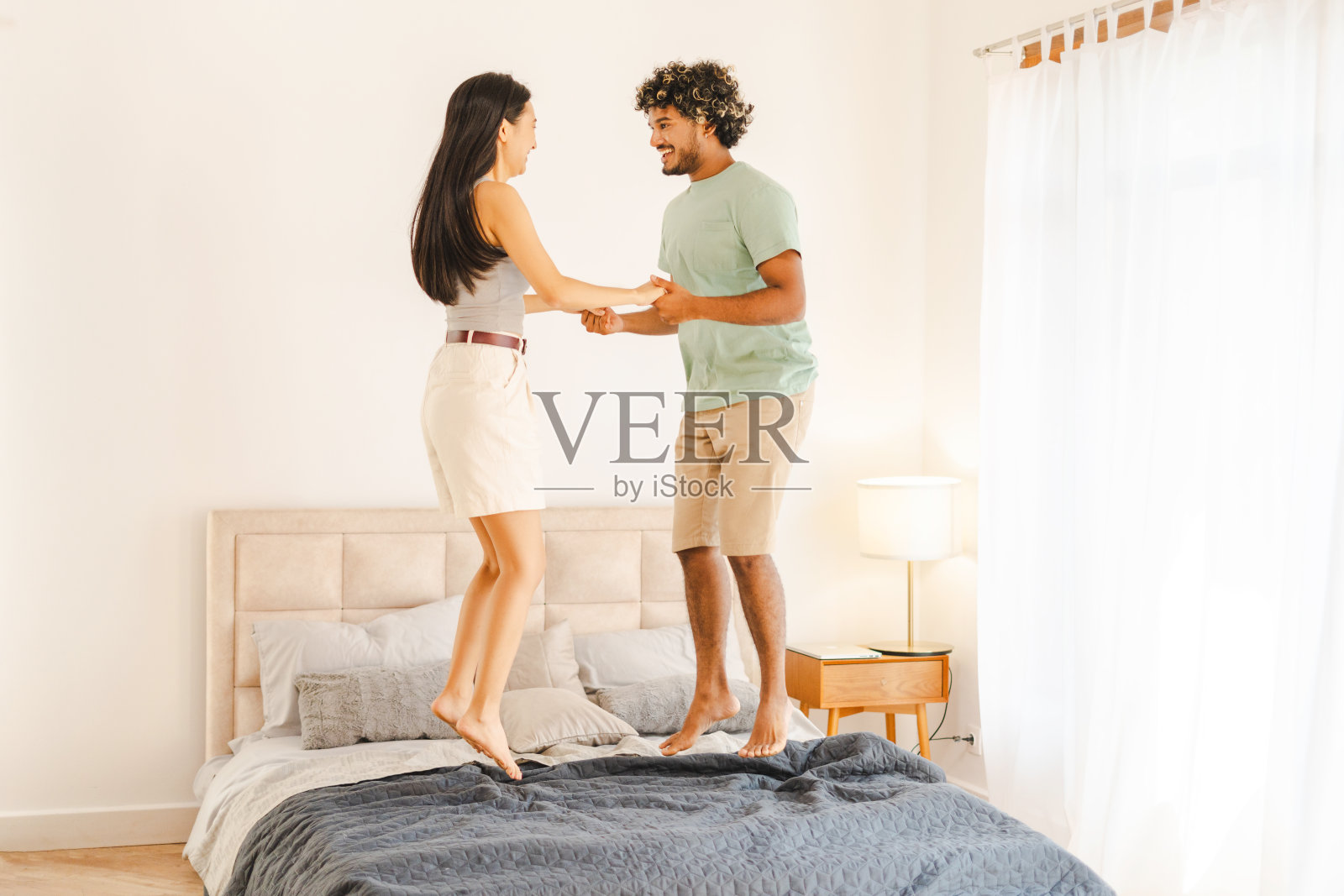 幸福的夫妻手牵着手，在床上跳来跳去，在家里玩得很开心照片摄影图片