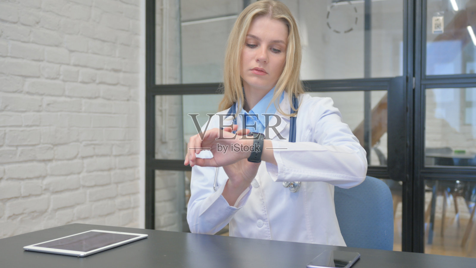 年轻的金发医生在诊所使用智能手表照片摄影图片