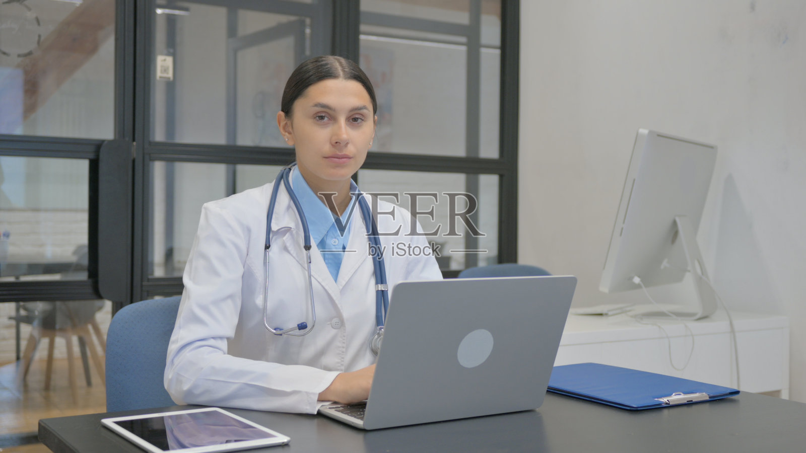 女医生一边用笔记本电脑工作一边看着相机照片摄影图片