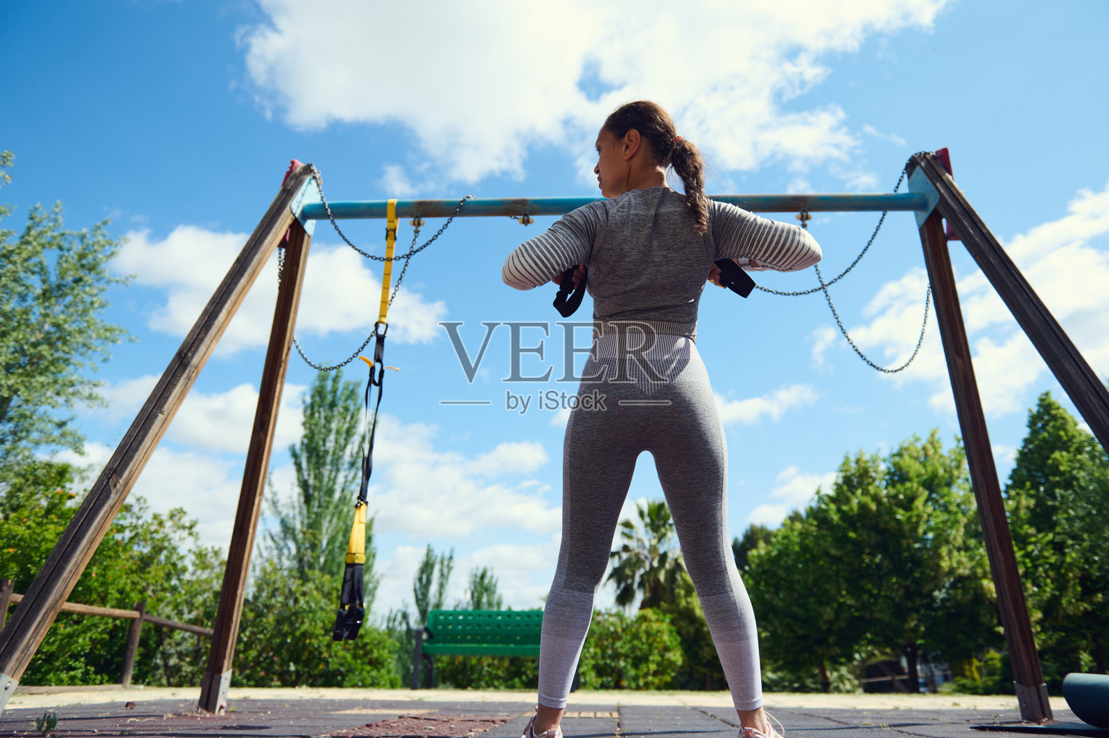 年轻女人在公园的阳光下用阻力训练器锻炼，专注于健身和力量训练照片摄影图片