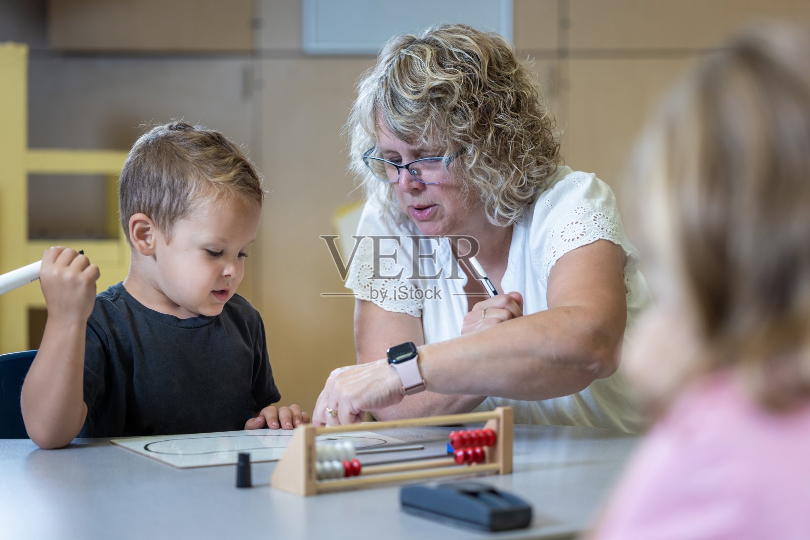 一个小男孩坐在桌子旁，他的老师正在教他数学照片摄影图片
