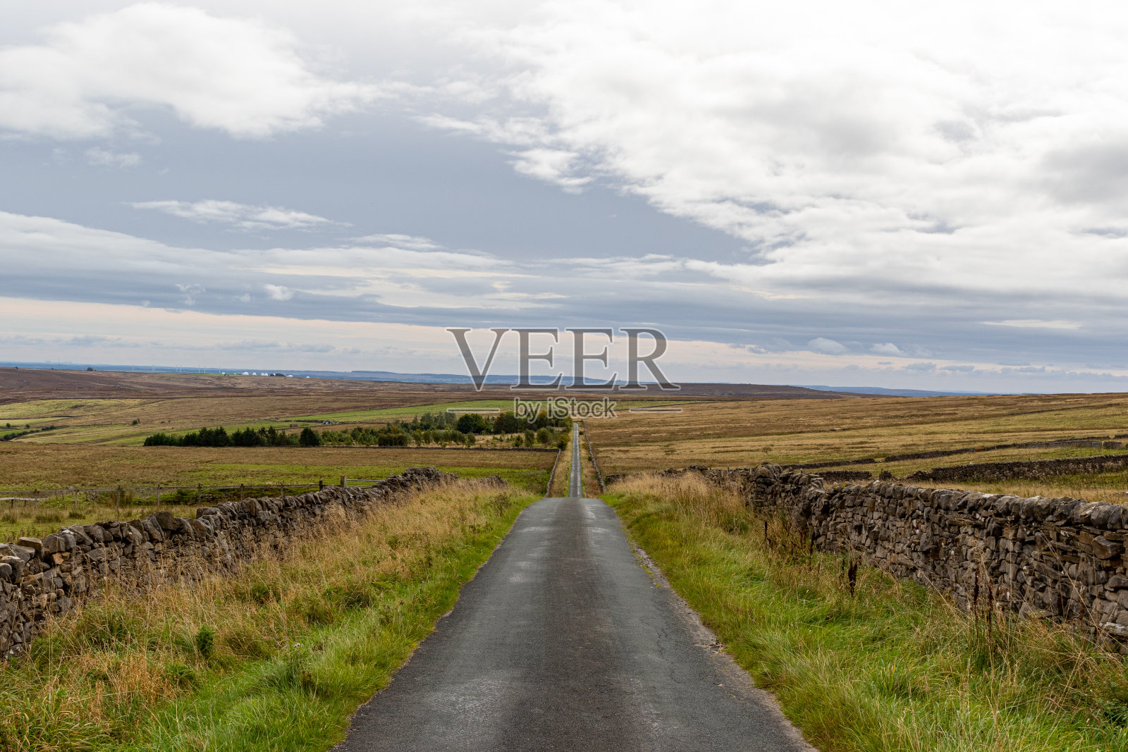 空旷的乡间小路，两边都是石墙，在多云的天空下通向广阔的沼地。照片摄影图片