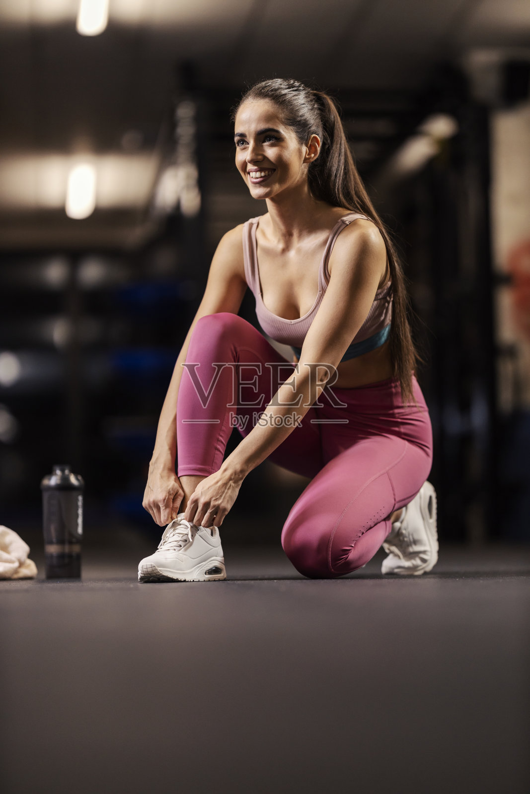 健身房里，一位身材健美的女运动员正在打鞋带。照片摄影图片