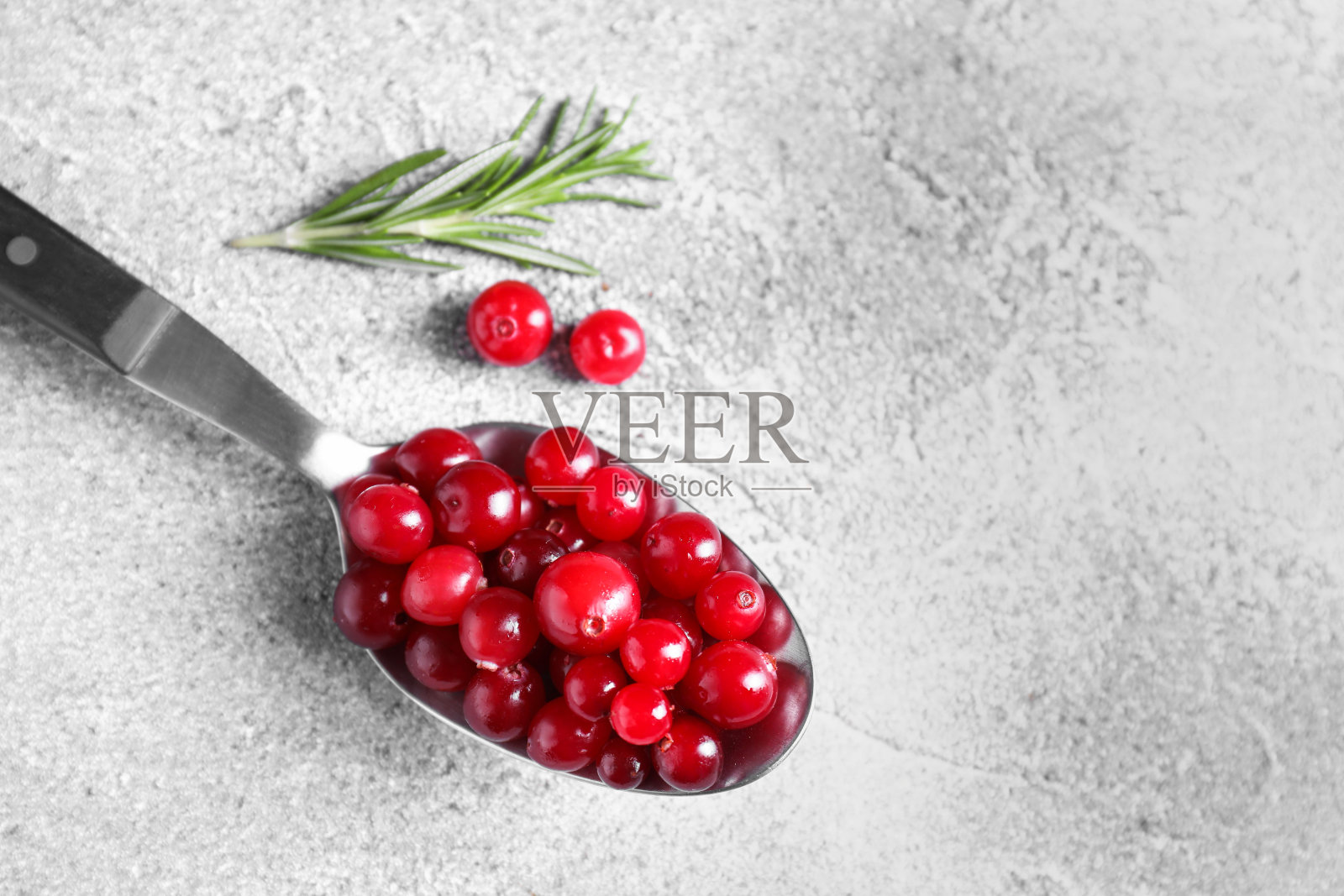 用勺子盛着新鲜成熟的蔓越莓，放在灰色的桌子上，特写。文本空间照片摄影图片