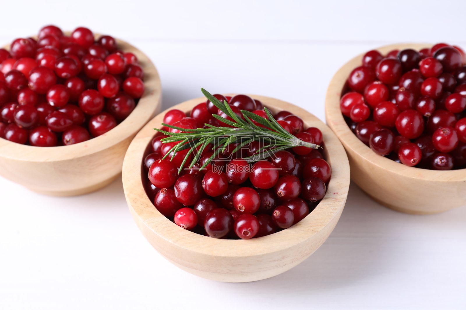 碗里盛着新鲜成熟的蔓越莓，白色木桌上放着迷迭香，特写照片摄影图片
