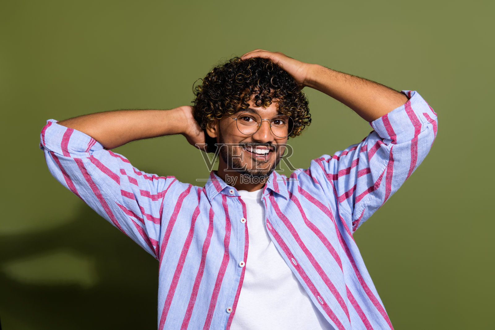 照片帅气酷的家伙波浪发型穿着条纹衬衫，眼镜触摸发型孤立的卡其色背景照片摄影图片