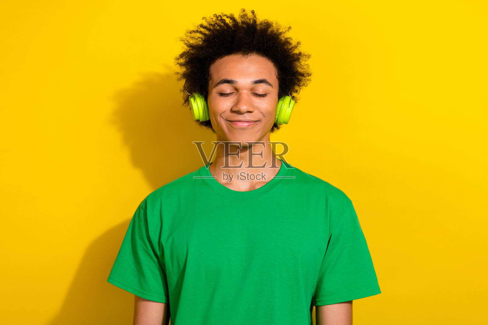 照片中有魅力的搞笑小伙戴着绿色的t恤耳机享受着歌曲空旷的空间孤立的黄色背景照片摄影图片