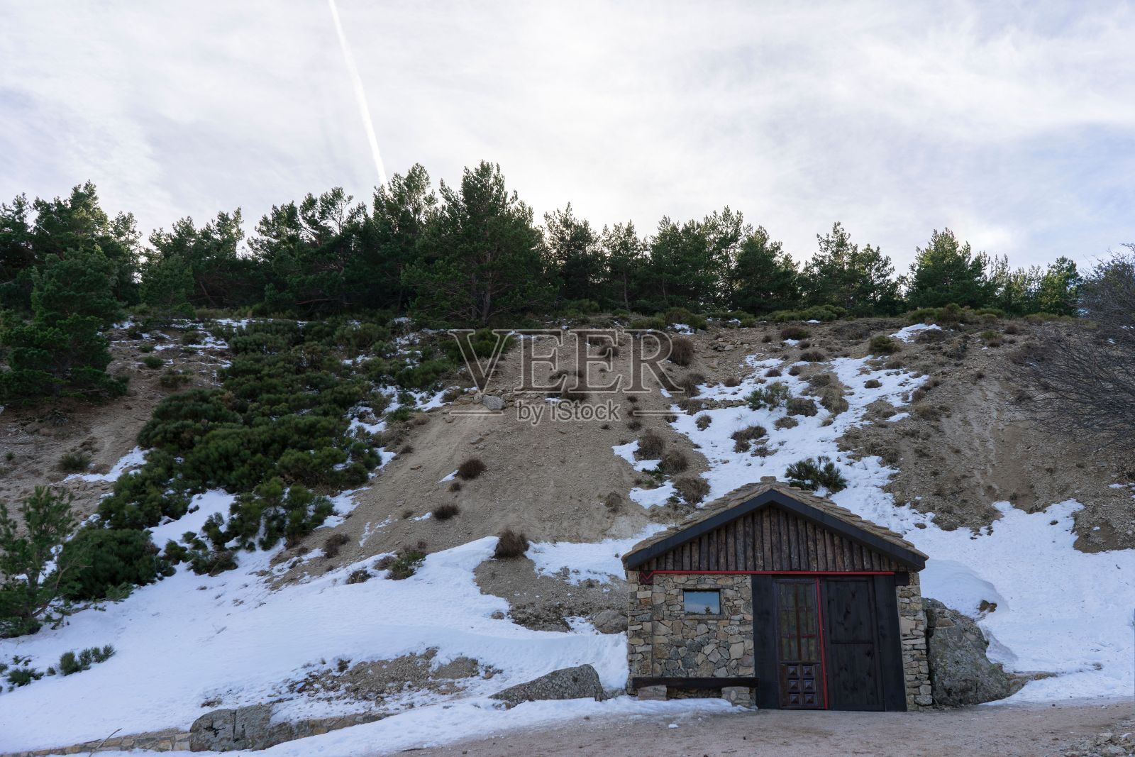 一间小石屋，有一扇木门，坐落在积雪的山坡上。照片摄影图片