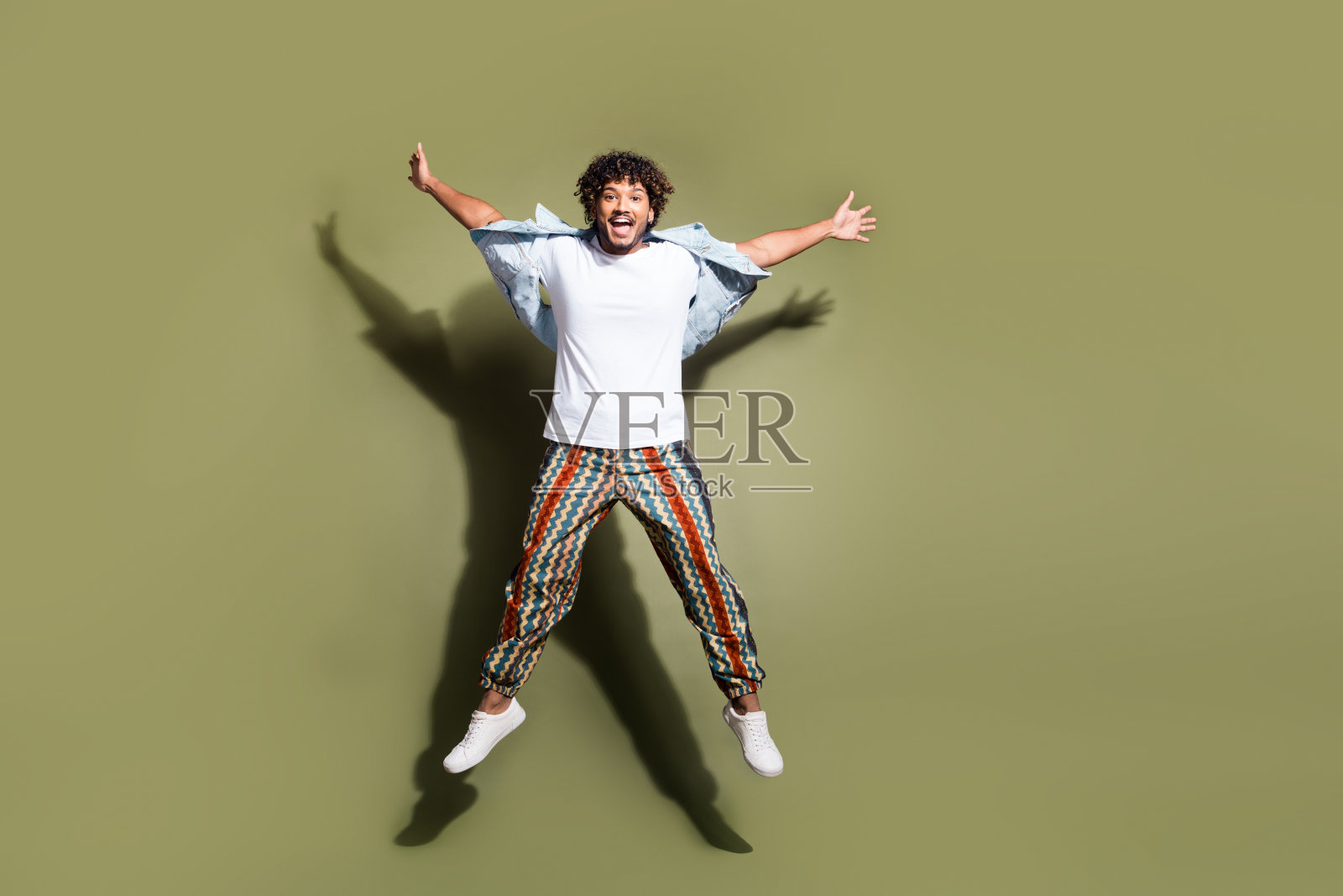 全尺寸照片英俊的年轻人跳伸展手腿穿时髦的牛仔裤服装孤立的卡其色背景照片摄影图片