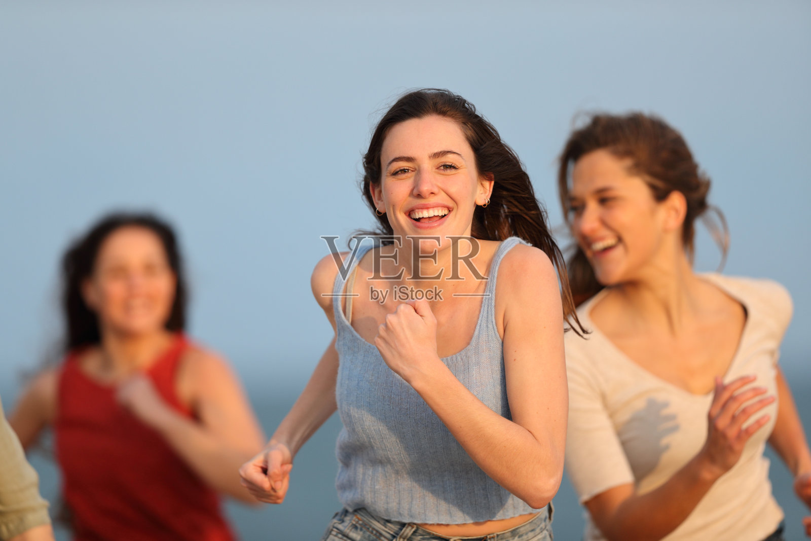 三个快乐的朋友在沙滩上跑步，享受假期照片摄影图片