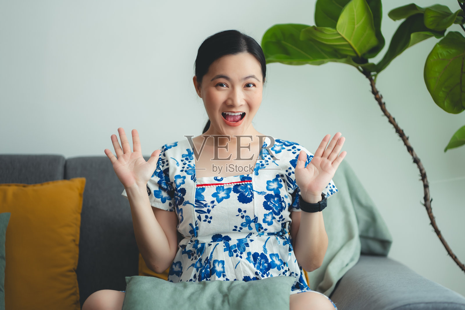 亚洲孕妇开心地微笑着兴奋地坐在家里客厅的沙发上，看着镜头。照片摄影图片