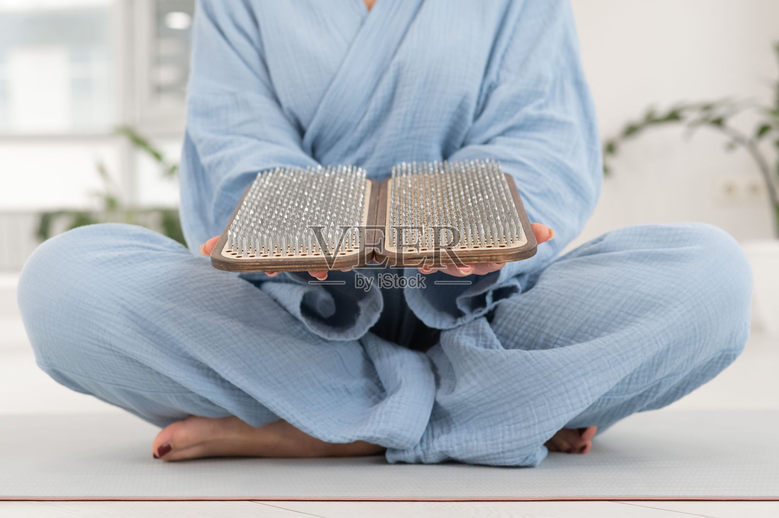 亚洲妇女在瑜伽垫上以莲花的姿势坐着，拿着瑜伽板。照片摄影图片