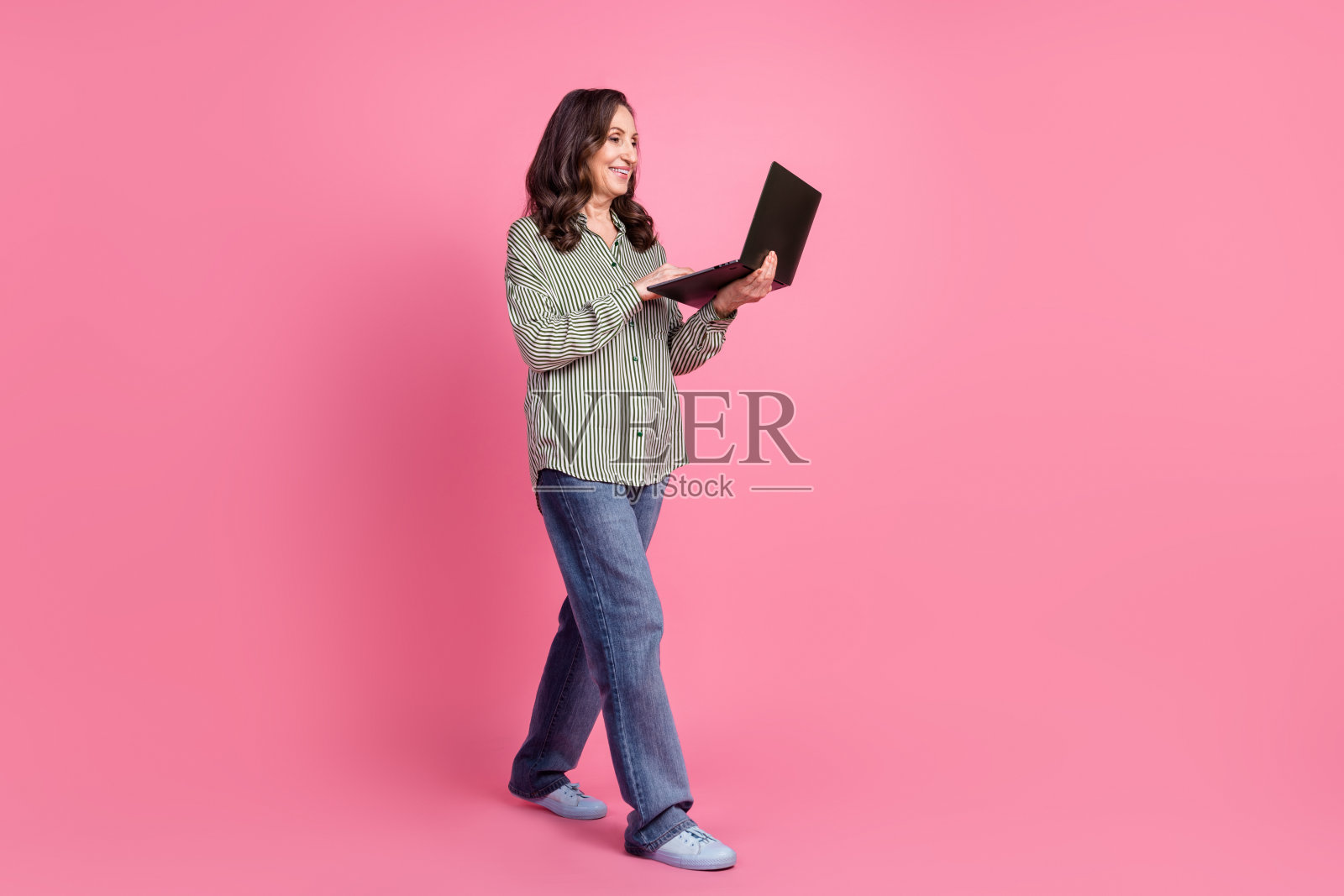 漂亮老太太的全身肖像走路用笔记本电脑穿衬衫孤立的粉红色背景照片摄影图片
