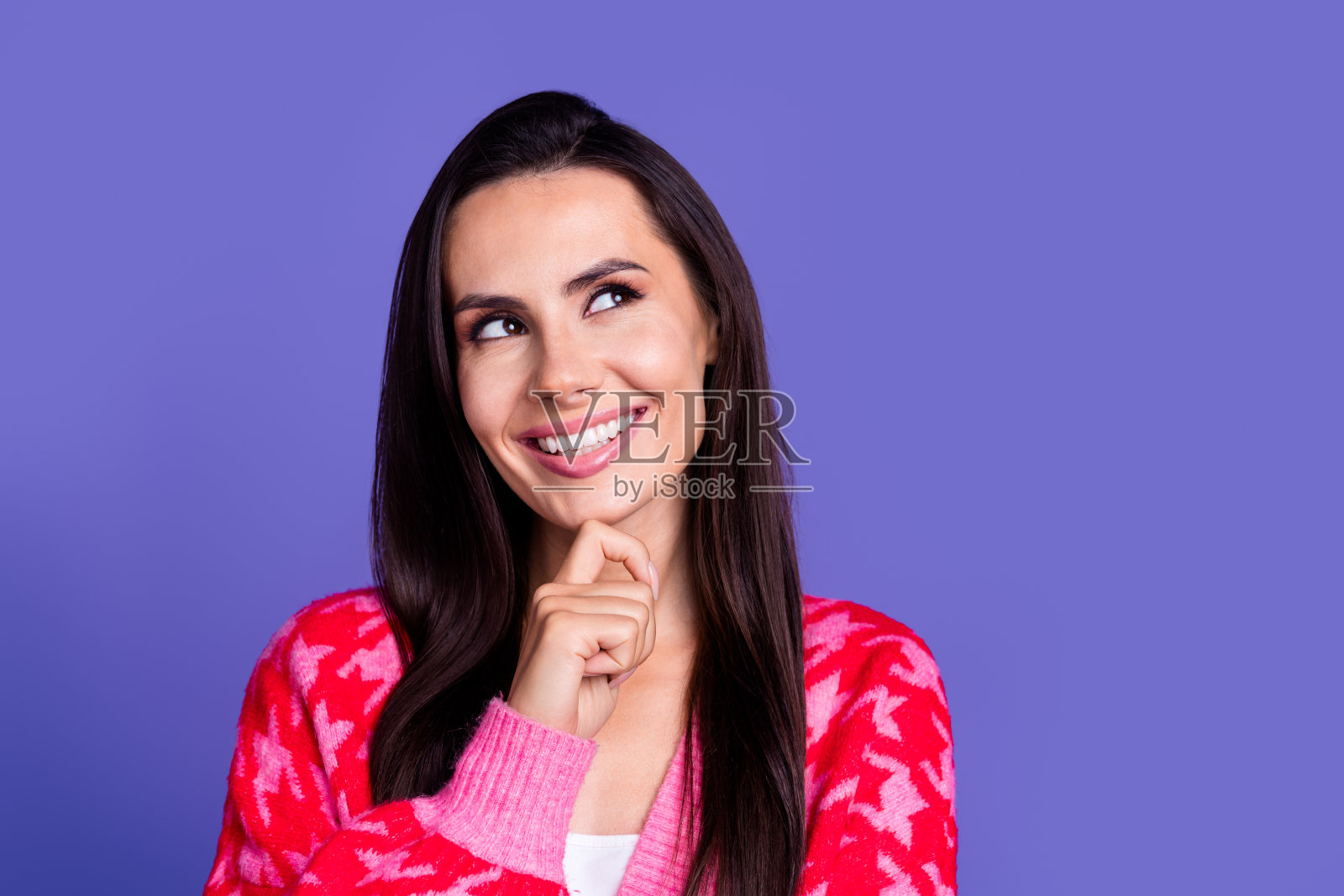 照片中开朗漂亮的女人穿着时髦的印花衣服，手臂触摸脸，在紫色的背景上看起来空无一物照片摄影图片