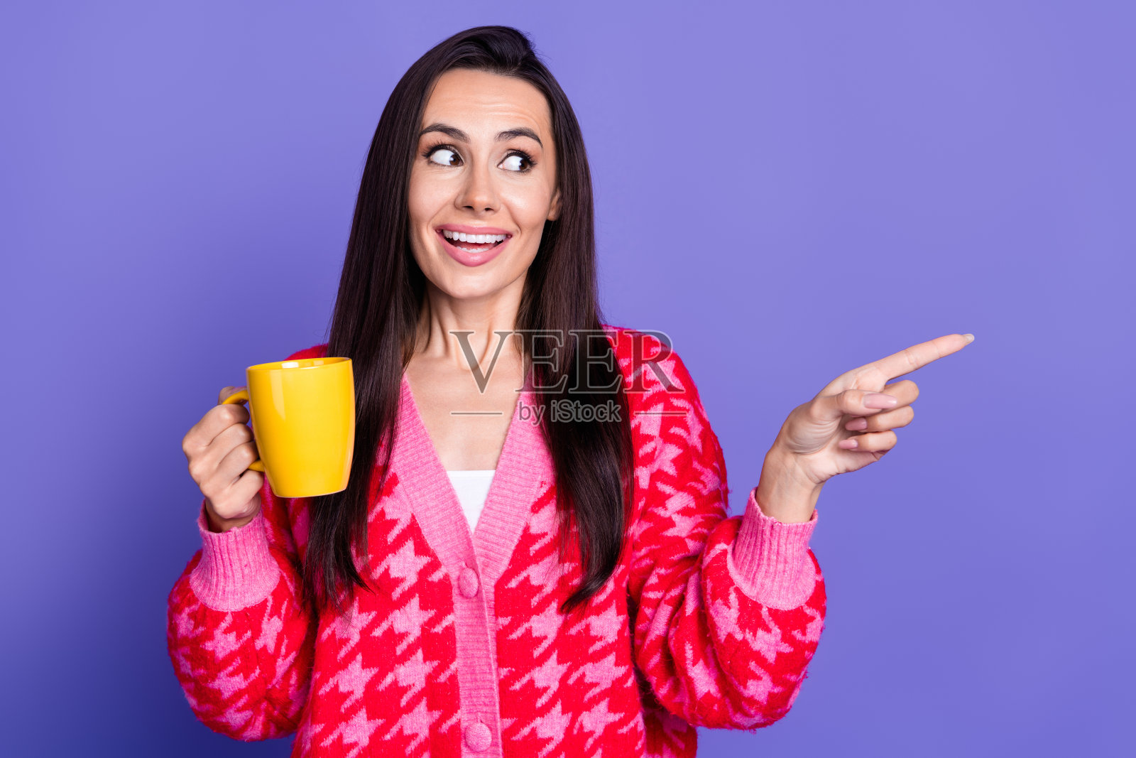 照片中兴奋迷人的女士穿着粉红色的开襟羊毛衫喝着饮料指着空旷的空间孤立的紫罗兰色背景照片摄影图片