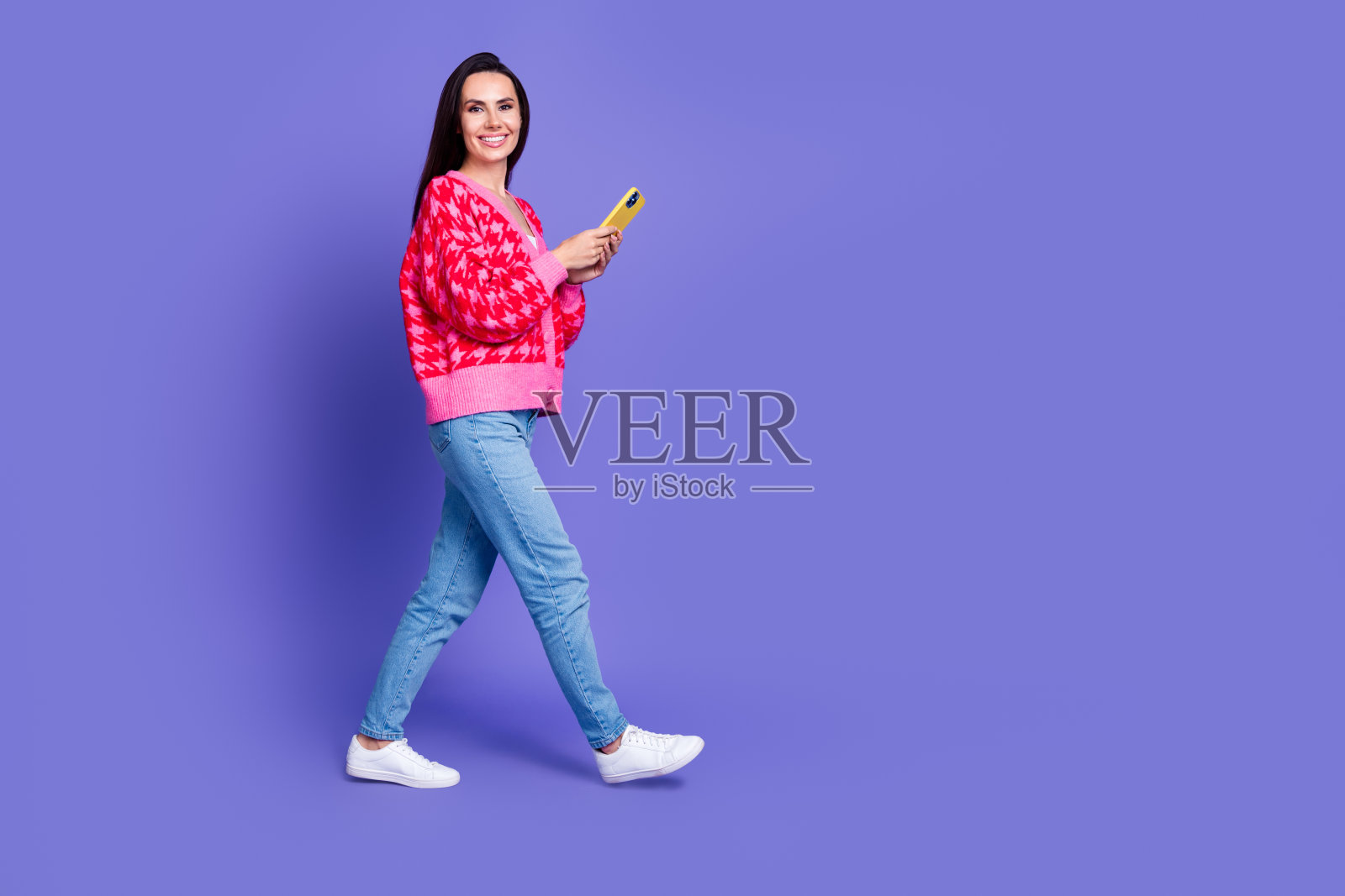 迷人的积极的女人穿着粉红色的开襟毛衣阅读现代小工具走空空间孤立的紫色背景的全长照片照片摄影图片