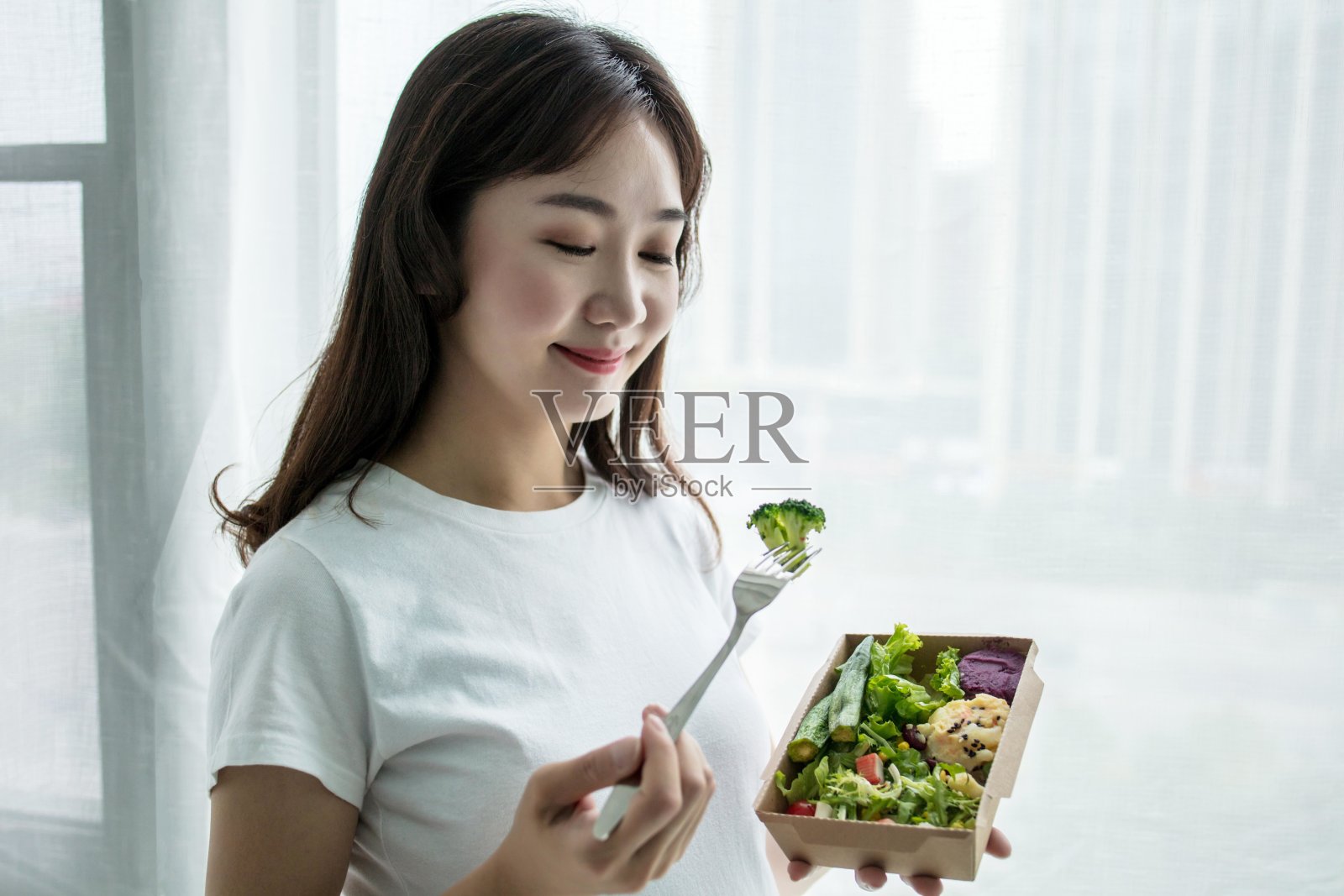 一名亚洲妇女正在吃含有西兰花、生菜和西红柿的健康沙拉照片摄影图片