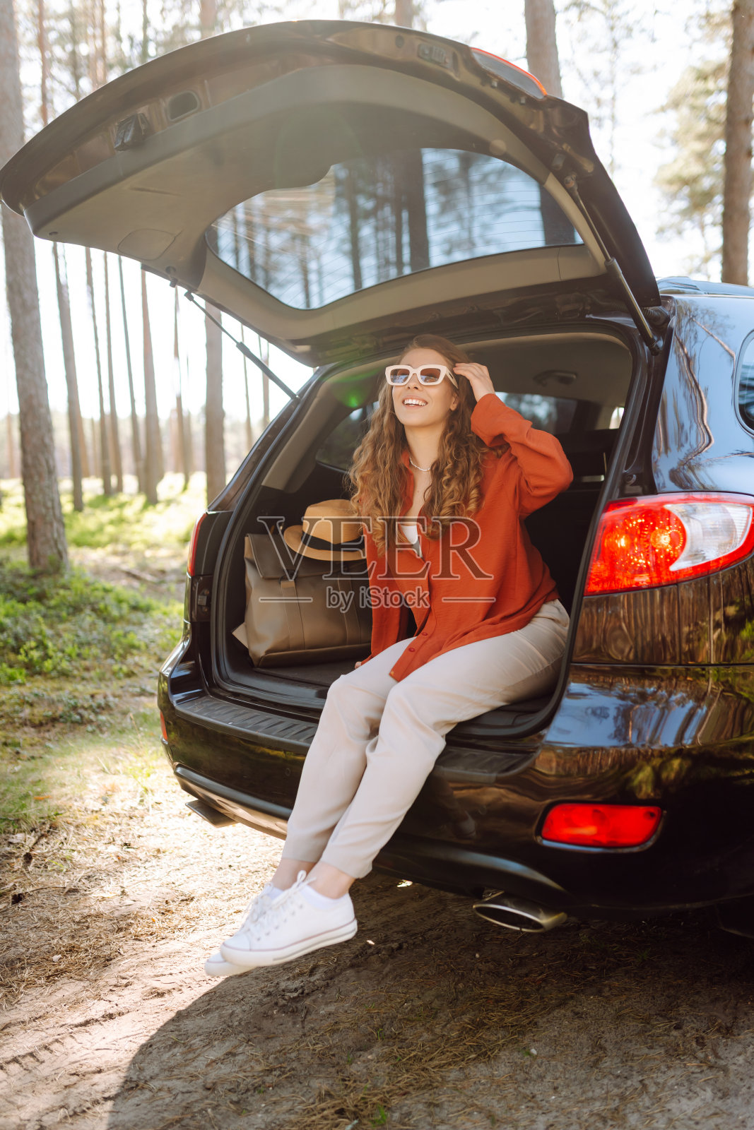 独自旅行时，一个快乐的女人坐在车的后备箱里享受大自然。照片摄影图片