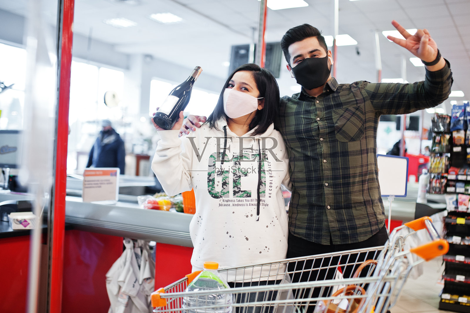 疫情期间，亚洲夫妇戴防护口罩在超市一起购物，挑选葡萄酒照片摄影图片