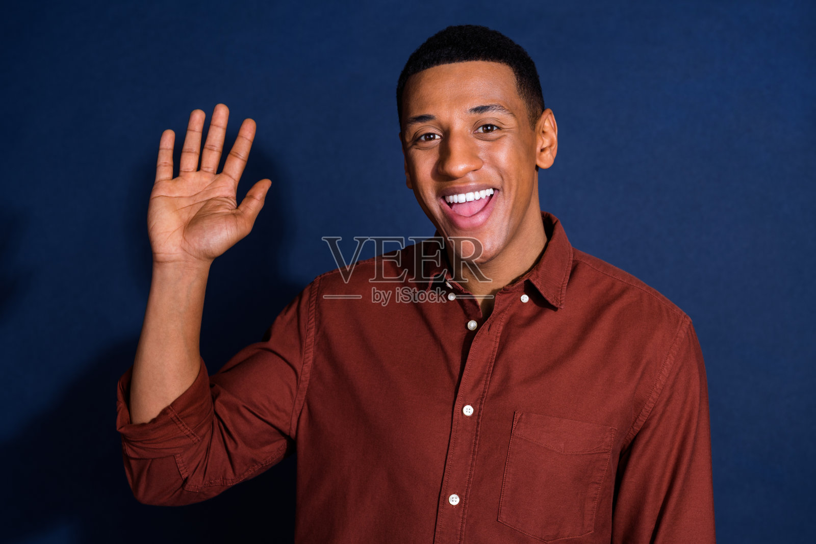 照片肖像英俊的年轻人挥手打招呼，穿着时尚的棕色服装孤立在深蓝色的背景照片摄影图片