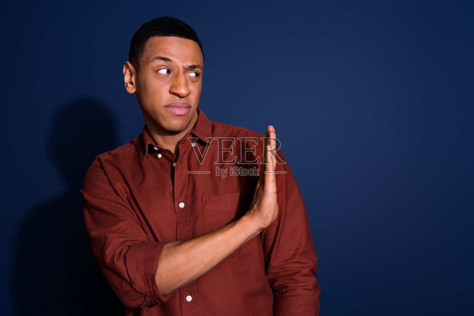 英俊年轻男子面露嫌弃表情，身着时尚棕色服装，深蓝色背景肖像照照片摄影图片