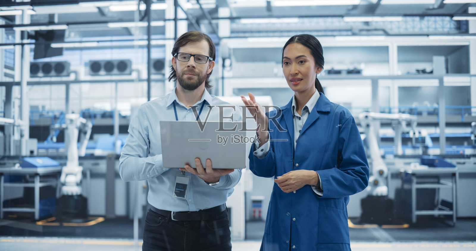 白人男性和亚洲女性在工业设施里交谈。先进工厂员工协同工作，使用笔记本电脑监督现代化工厂的工作过程照片摄影图片