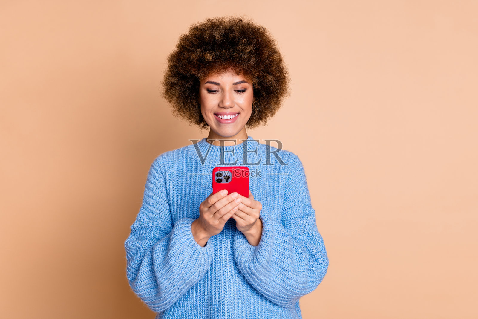 照片中开朗友好的女孩穿着蓝色针织毛衣，看着智能手机，阅读电子邮件，孤立在柔和的颜色背景照片摄影图片