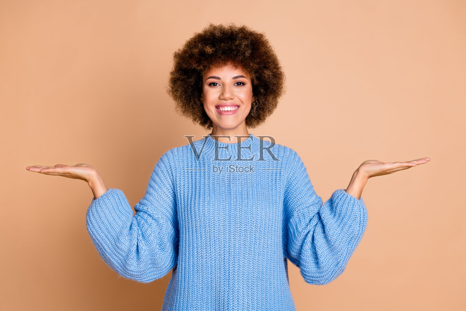 照片积极开朗的女孩穿着蓝色针织毛衣比较产品在手掌空空间孤立在柔和的颜色背景照片摄影图片