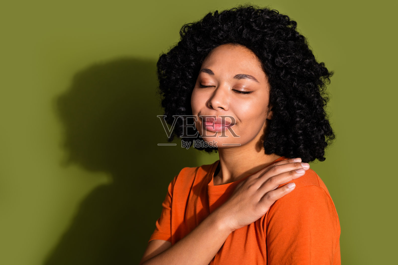 照片中漂亮的年轻女子闭着眼睛碰着肩膀，穿着橙色t恤孤立在卡其色背景上照片摄影图片