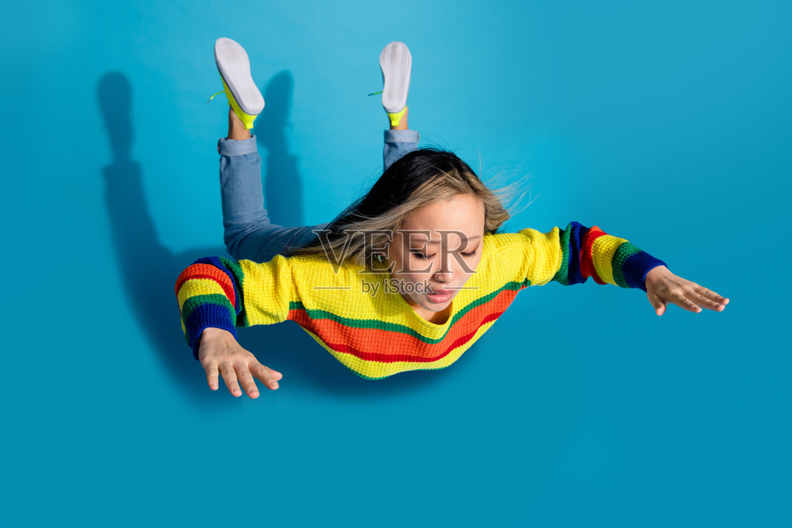 可爱的年轻女士摔倒的全身照片，穿着时尚的条纹服装，孤立在蓝色背景上照片摄影图片