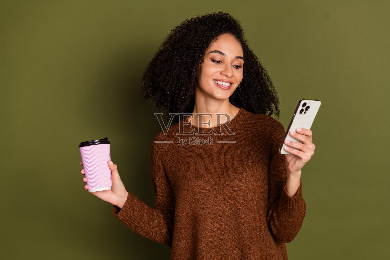 漂亮的年轻女子的肖像智能手机咖啡穿毛衣孤立的卡其色背景照片摄影图片