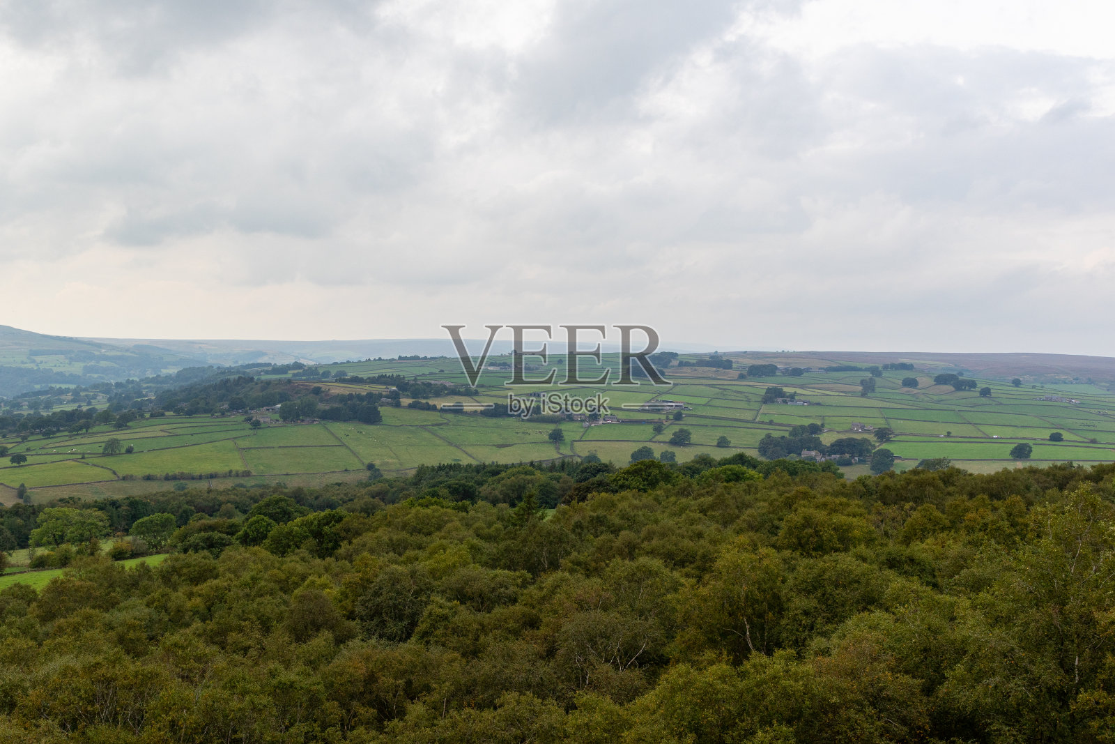 在多云的天空下，连绵起伏的青山和郁郁葱葱的树木，描绘了北约克郡布里姆岩石宁静的乡村景观。照片摄影图片
