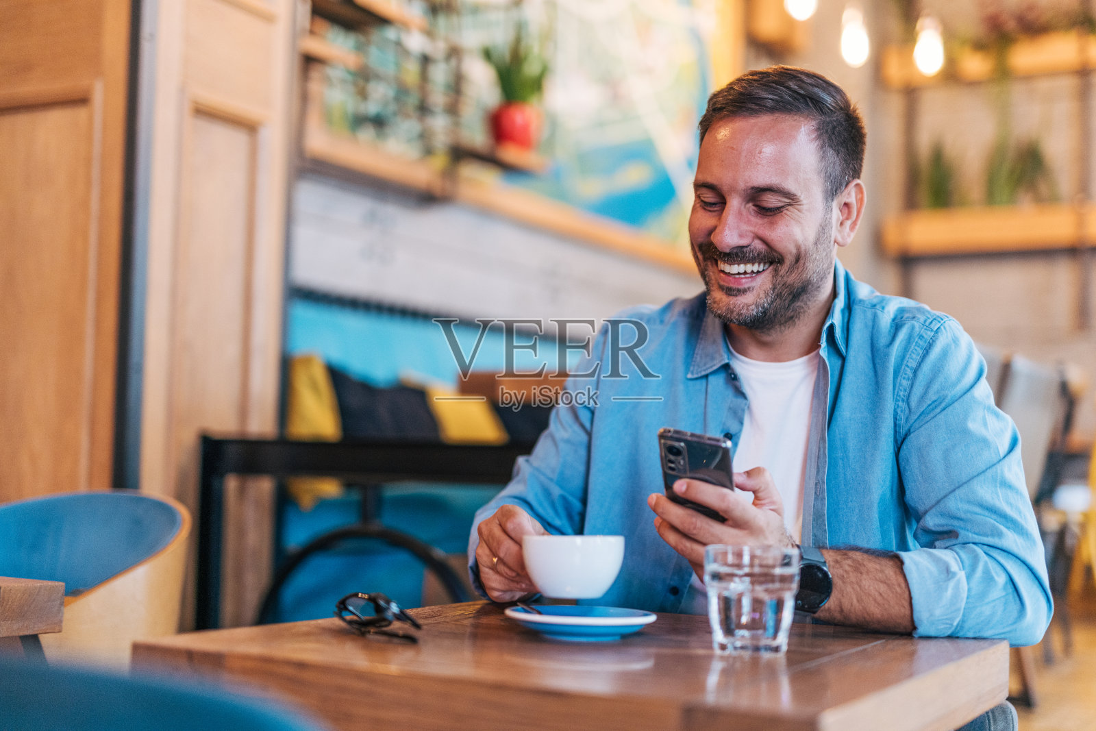快乐英俊的中年男子在咖啡馆享受宁静的咖啡休息时间，并使用智能手机照片摄影图片