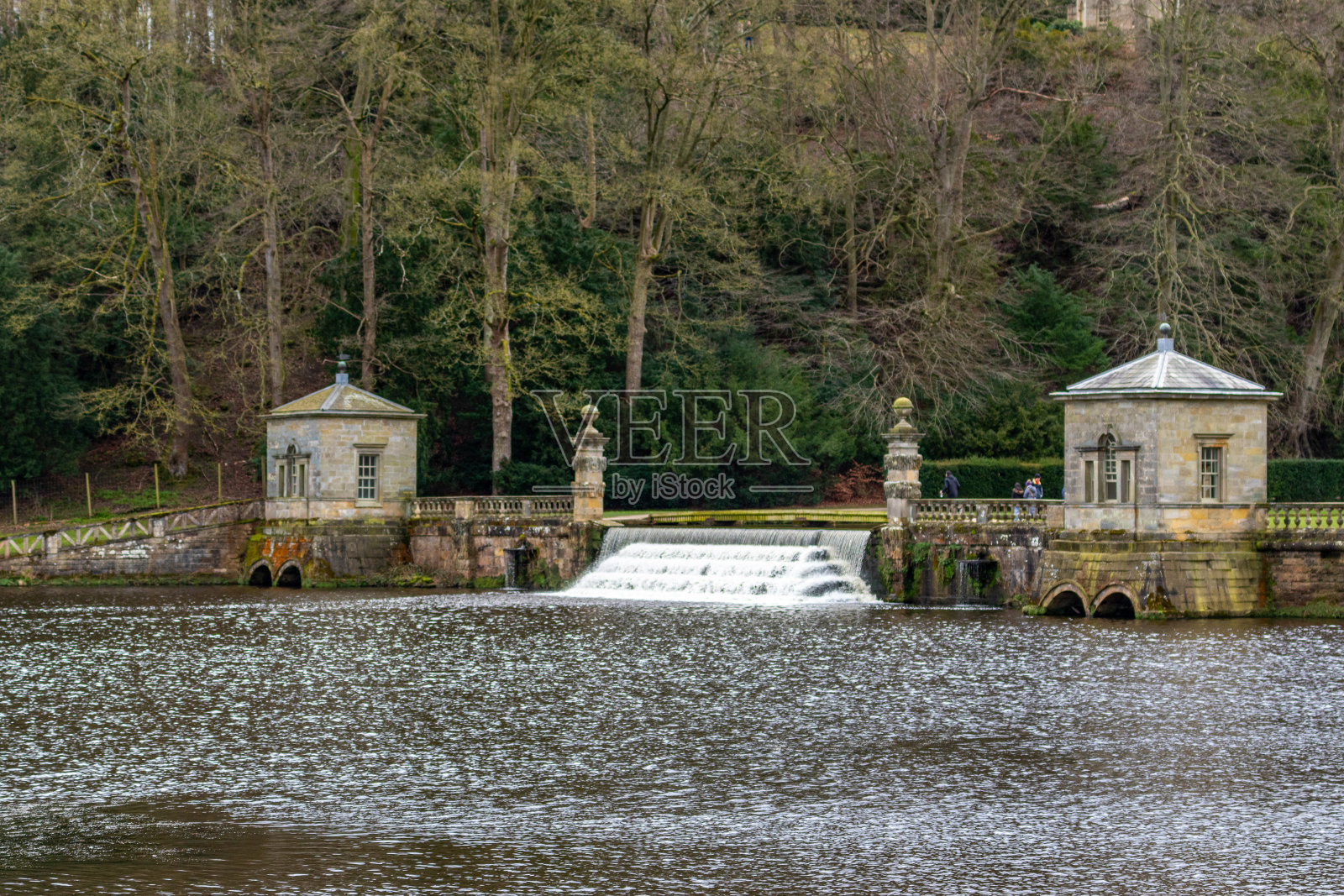 历史悠久的石头建筑，河边有一个小瀑布和郁郁葱葱的绿色背景。照片摄影图片