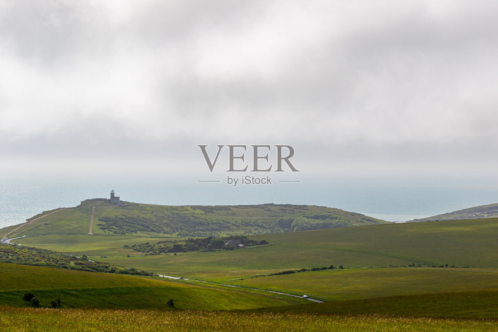 连绵起伏的青山和远处的高塔在多云的天空下，英国七姐妹。照片摄影图片