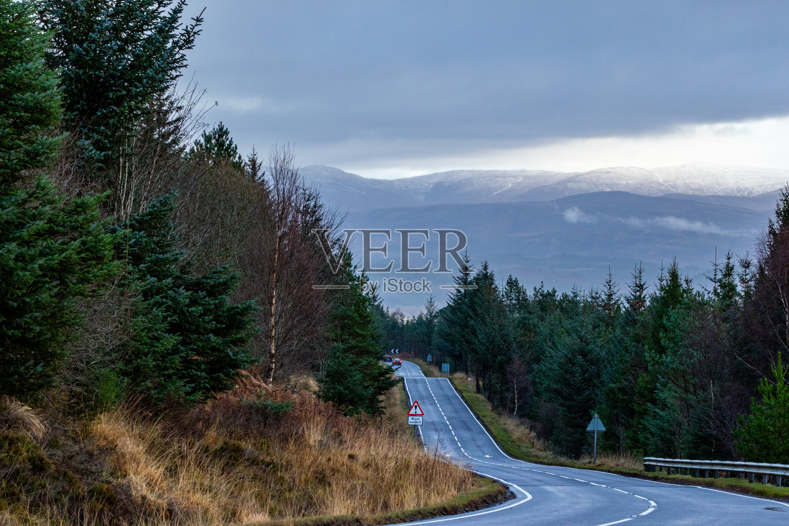 在苏格兰的一个阴天，风景优美的蜿蜒道路穿过森林，背景是雾蒙蒙的山脉。照片摄影图片