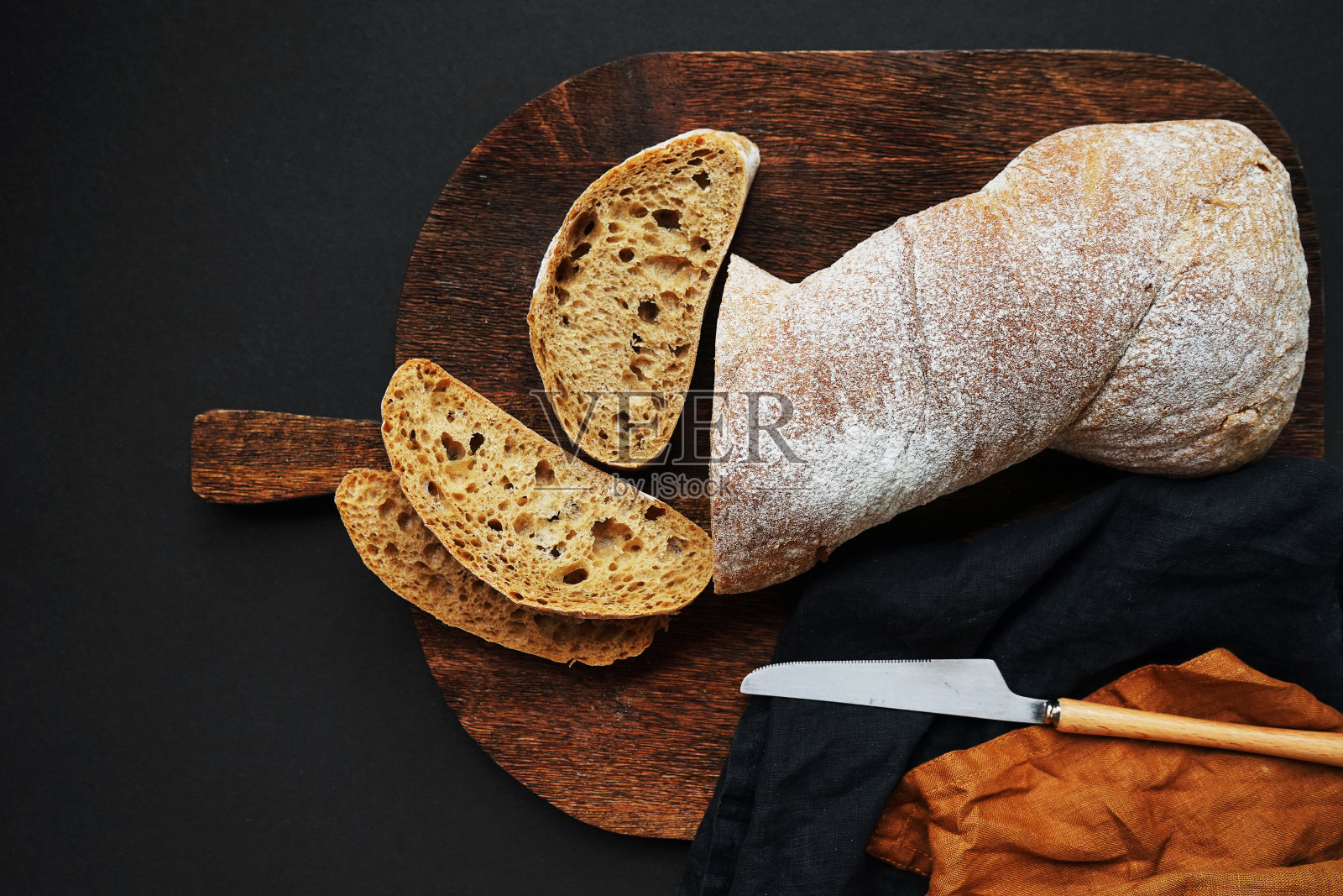 新鲜切片的面包放在木板上，旁边是一把刀和一张亚麻布餐巾照片摄影图片